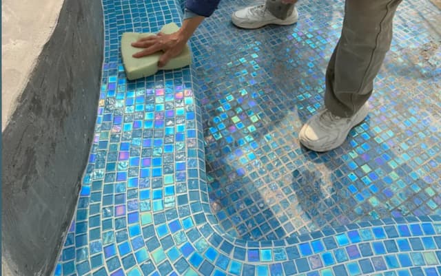 Blue iridescent mosaic floor tile following a curved pool transition during installation